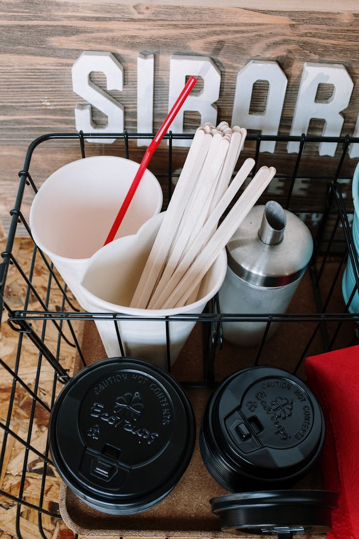 services-01 A collection of disposable coffee supplies inside a rustic café, featuring cups, lids, and stirrers.