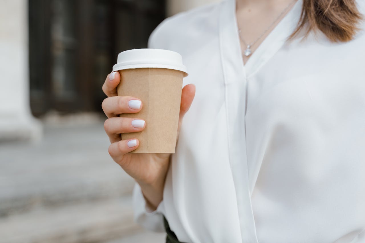 Close-up of a woman in a white blouse holding a paper coffee cup.